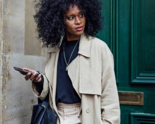 A stylish mid adult woman leaving her house in Newcastle upon Tyne, England. She is standing in front of her front door, using her phone while looking to her side with a contented look on her face as she heads off to work.