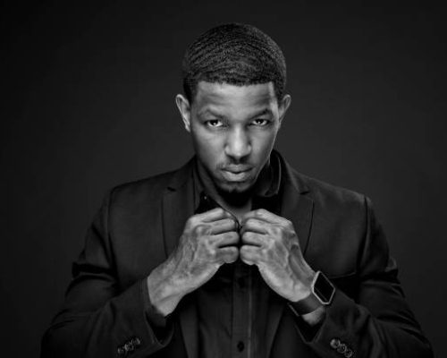 Portrait Of Serious Male Model Buttoning Shirt While Standing Against Black Background